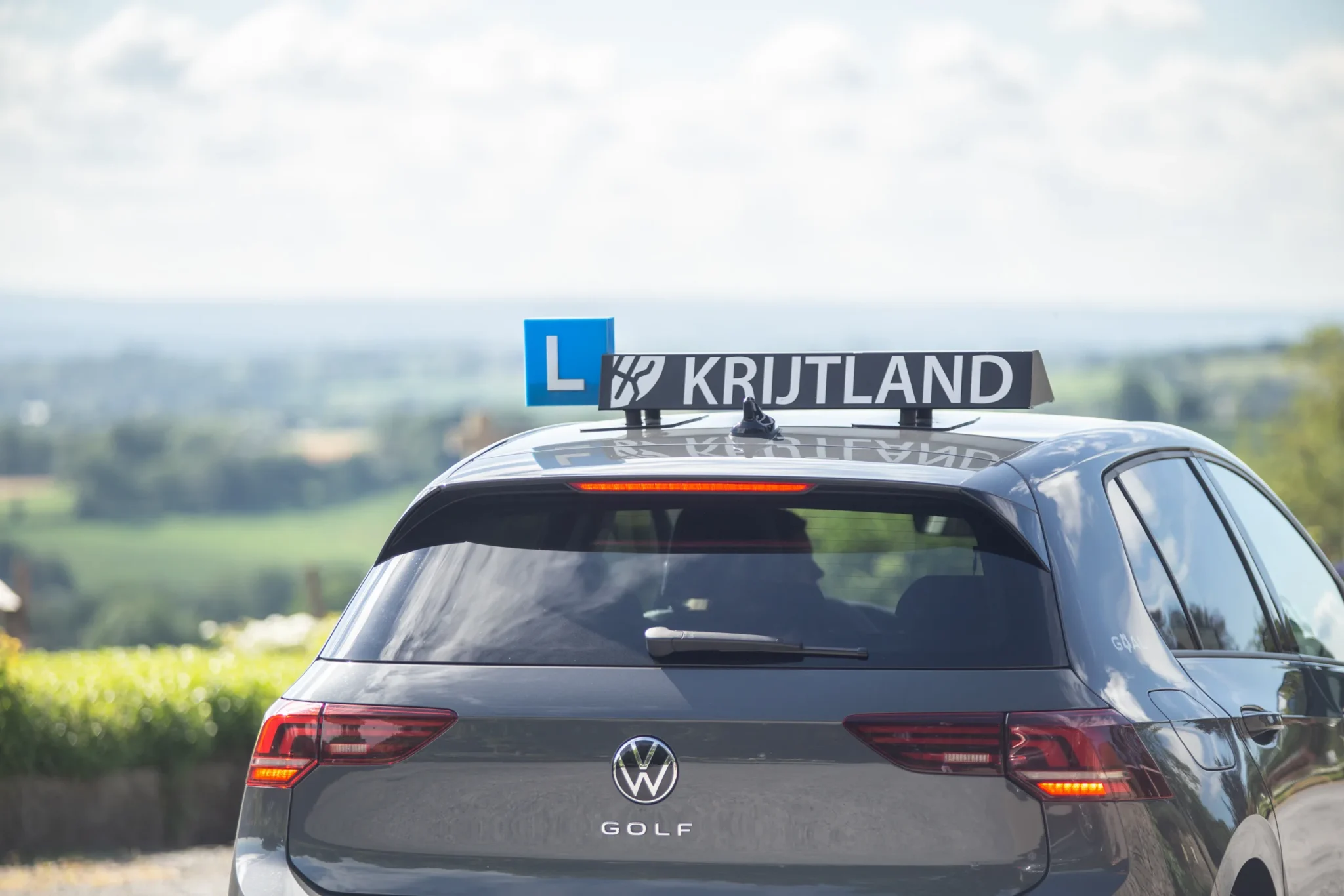 Leerling stapt in de lesauto met uitzicht over het Limburgse heuvelland